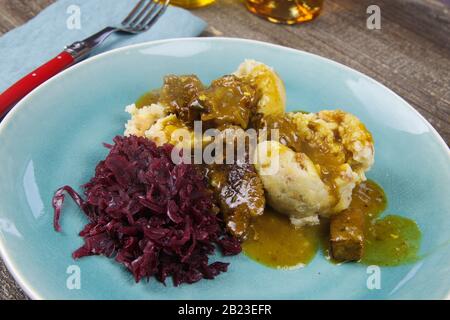 Pasto tipico tedesco abbondante: Closeup di gnocchi con salsa marrone, cavolo rosso, carne di goulash su piatto blu della cina Foto Stock