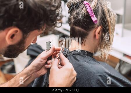 Il parrucchiere principale taglia i capelli della donna bionda nel salone. Chiudi la foto. Foto Stock