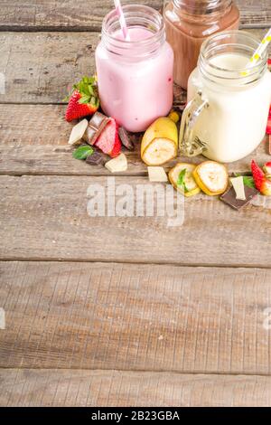 Tre vasetti da muratore con milkshake o frullato. Colazione estiva sana, pranzo bevande - banana, cioccolato e fragole milkshake su backgroun in legno Foto Stock