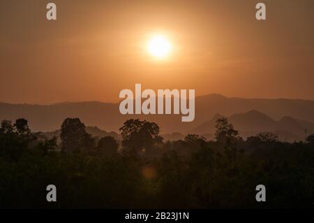 Silhouette di alberi e montagne stratificate in una luce arancione con un tramonto sullo sfondo nella regione tailandese di Khao Yai Foto Stock