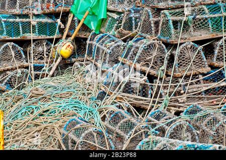 Creels, o granchi pentole, accatastati sul lato del quayside con corde e bandiere di posizione fluttuanti. Foto Stock