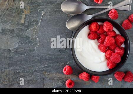 Ciotola di yogurt con lamponi. Vista dall'alto, bordo laterale su sfondo scuro in ardesia. Spazio di copia. Foto Stock