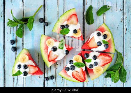 Pizza al cocomero con mirtilli, fragole, banane, menta e yogurt. Vista dall'alto su uno sfondo rustico di legno blu. Foto Stock