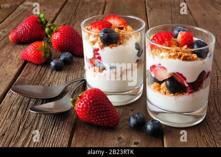 Parfaits fragola e mirtillo in bicchieri contro uno sfondo rustico di legno scuro Foto Stock