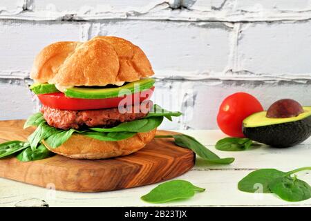 Hamburger senza carne a base di piante con avocado, pomodoro e spinaci su una tavola da tavola in legno su uno sfondo bianco di mattoni Foto Stock