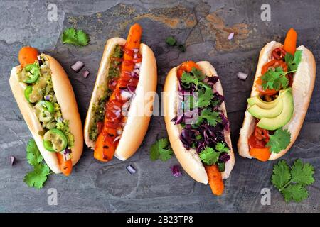 Hot dog vegan alla carota con guarnizioni assortite. Sopra la scena di vista su uno sfondo scuro di ardesia. Concetto di pasto senza pasto a base di piante. Foto Stock