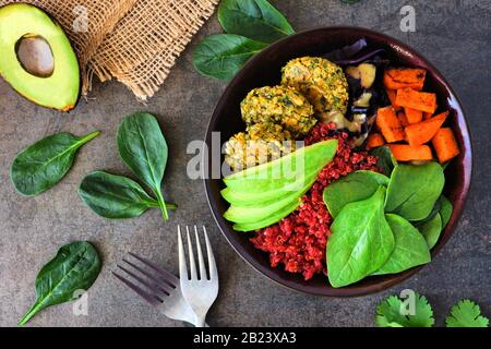 Ciotola sana di buddha vegano con falafel, quinoa di barbabietola, avocado, e verdure su uno sfondo di pietra scura. Concetto di alimentazione sana. Scena aerea. Foto Stock