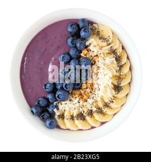 Ciotola di frullato di mirtillo sano con noce di cocco, banane, semi di chia e granola isolato su uno sfondo bianco Foto Stock