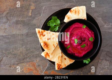 Hummus di barbabietola tuffarsi con pane pita su una piastra nera, sopra la vista su uno sfondo scuro Foto Stock