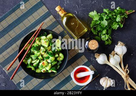 Insalata cinese di cetrioli Fracassati, pai huang gua, con salsa di soia all'olio di sesamo al peperoncino, cosparsa di foglie fresche di coriandolo in una ciotola nera o Foto Stock