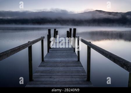 Hawse End jetty e misty riflessioni di colline lontane all'alba, Derwentwater, Lake District National Park, Cumbria, Inghilterra, Regno Unito Foto Stock