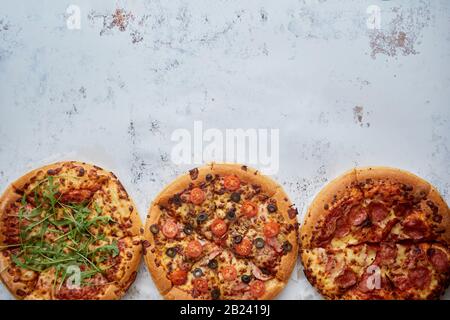 Tre diversi tipi di pizze messo in fila sul bianco tavolo arrugginita Foto Stock