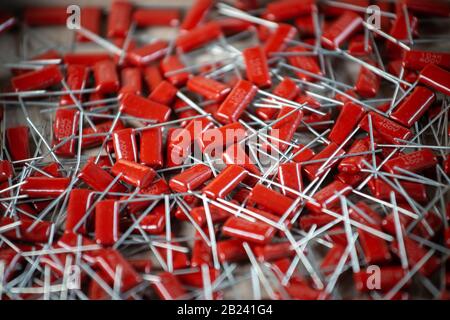 Il primo piano di un gruppo di condensatori rossi si trova l'uno sopra l'altro in una fabbrica di computer e apparecchiature per ufficio. Concetto di parti di qualità. Lotto all'ingrosso Foto Stock