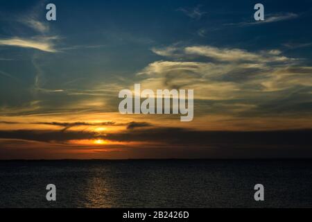 Un tramonto su più strati e multicolore sull'acqua con alte nuvole bianche e riflessi Foto Stock