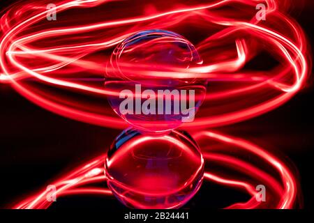 gli anelli rossi circondano una sfera di vetro trasparente su uno specchio Foto Stock