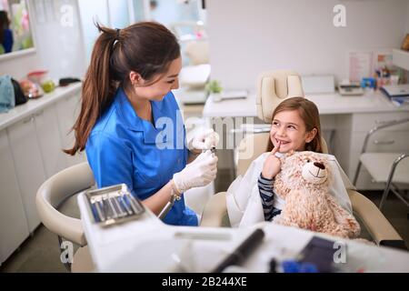 Ragazza sorridente in sedia dentale mostrando dente al dentista Foto Stock