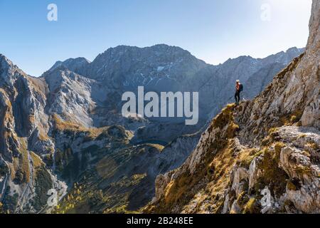 Alpinista con casco da arrampicata si erge su uno sperone roccioso, sentiero escursionistico per Ehrwalder Sonnenspitze, Ehrwald, Mieminger Kette, Tirolo, Austria Foto Stock