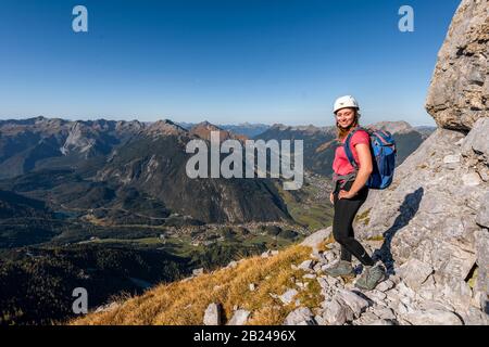 Giovane donna, alpinista con casco da arrampicata guardando il paesaggio di montagna, escursione a Ehrwalder Sonnenspitze, dietro Gruenstein e ovest Foto Stock