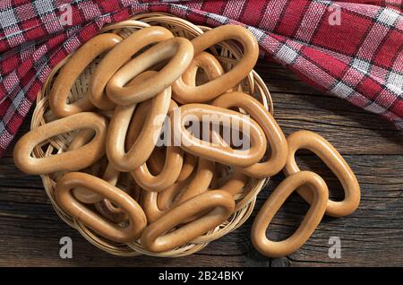 Gustosi bagel ovali in ciotola piatto di vimini su un tavolo rustico in legno, vista dall'alto Foto Stock