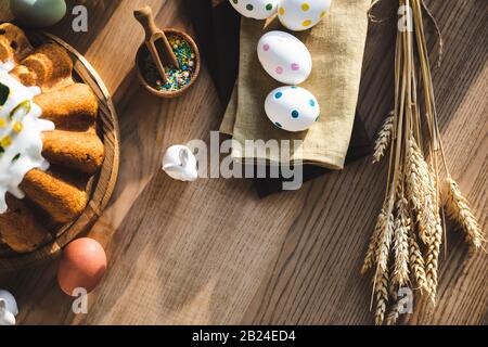 vista dall'alto della torta di pasqua vicino alle uova punteggiate su tovaglioli di lino, figurine con conigli e grano Foto Stock