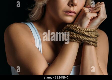 Vista corta della donna con le mani legate vicino al viso isolato sul nero Foto Stock