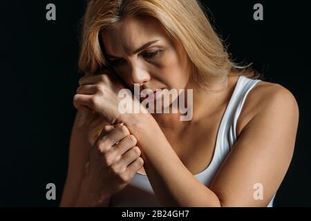 Donna premurosa e sconvolta con la mano vicino al viso isolato sul nero Foto Stock