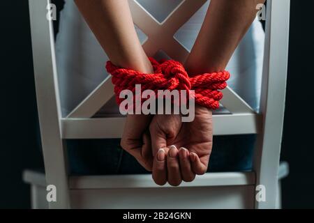 Vista corta delle mani femminili legate con corda rossa isolata su nero Foto Stock