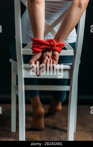 Vista corta della donna con le mani legate sulla sedia su sfondo nero Foto Stock