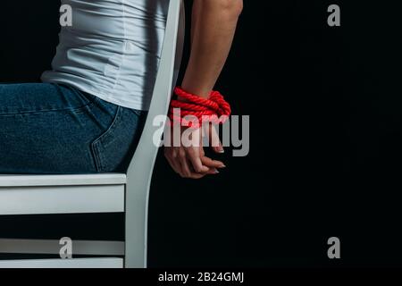 Vista corta della donna con legato mani sulla sedia isolato su nero Foto Stock