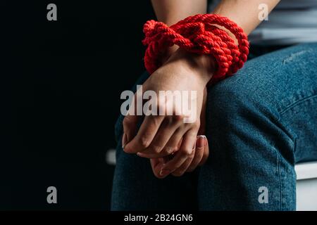 Vista ritagliata delle mani delle vittime legate con corda isolata su nero Foto Stock