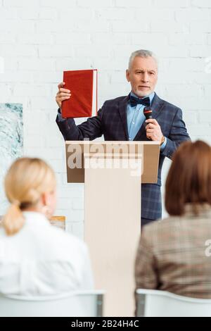 fuoco selettivo di auctioneer parlare con microfono e tenere libro durante l'asta Foto Stock