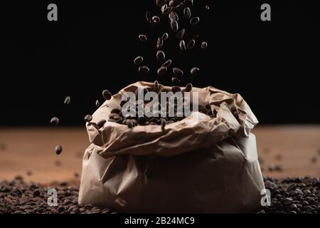 chicchi di caffè arrosto che cadono in borsa su sfondo nero Foto Stock