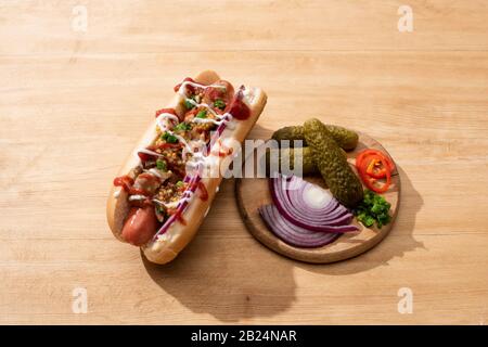 Delizioso cane caldo con cipolla rossa, pancetta e senape di Digione vicino a bordo con verdure su tavola di legno Foto Stock