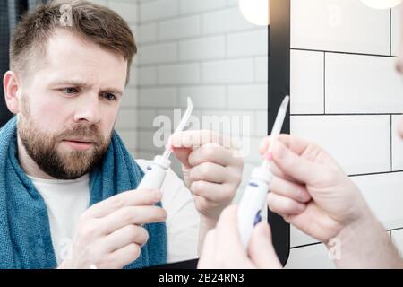 Riflessione nello specchio di un uomo concentrato che tiene in mano un irrigatore elettrico e cerca di capire come funziona. Foto Stock