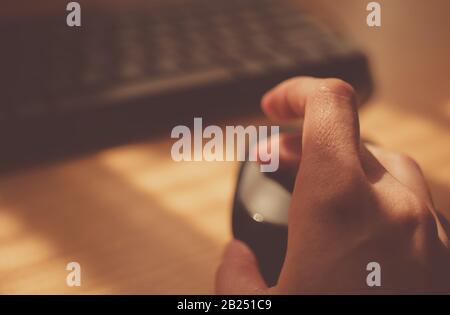 Mouse per computer per uso femminile vicino alla tastiera. Tavolo soleggiato con luce calda. Messa a fuoco selettiva sul dito Foto Stock