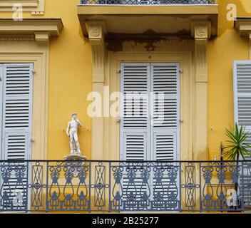 Vista dalla strada di grande balcone dipinto di giallo con statua antica e persiane a finestra chiusa Foto Stock