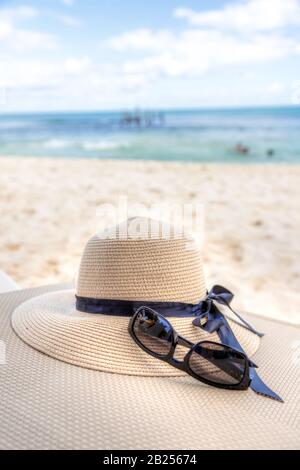 Tema vacanza con occhiali da sole e cappello in una spiaggia tropicale con mare e cielo blu. Spazio di copia. Foto Stock