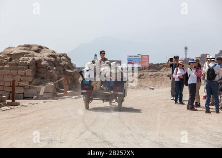 Pachacamac, Lima / PERÙ - 10 maggio 2016: Archeologo a cavallo su un moto taxi passato un gruppo di turisti in un sito archeologico a Pachacamac, Lima Perù. Foto Stock