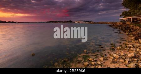 Tramonto di Crimson sopra Bramble Bay verso Sandbanks a Dorset con Brownsea Island visibile attraverso l'acqua Foto Stock