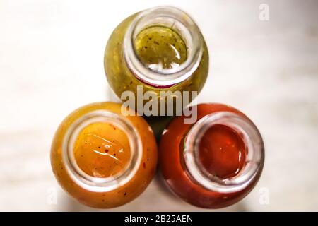Tre bottiglie di salse: Calde, tomatoe e erbe dall'alto. Foto Stock