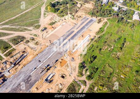 costruzione di una nuova strada urbana in periferia. macchine industriali pesanti in cantiere. vista aerea Foto Stock