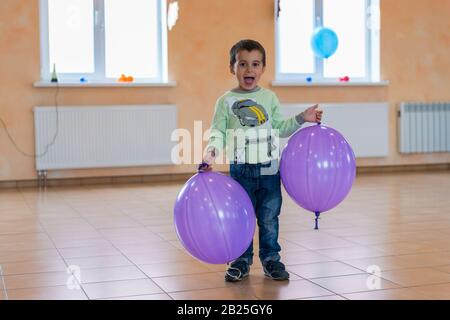 Ragazzino con grande palloncini. Capretto felice con palloncini viola nella hall. Foto Stock