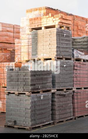 Diversi pallet con mattoni di cemento sovrapposti in magazzino. La produzione industriale di mattoni. foto verticale. Foto Stock