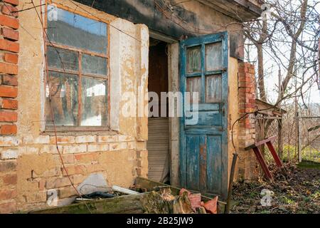 In stile retrò granaio o casa colonica in mattoni abbandonati con porte blu aperte e grande finestra in paese o campagna. Primo piano. All'Aperto. Foto Stock