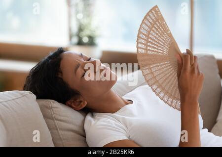 Donna biraciale esausta ondola con ventilatore a mano che soffre di colpo di calore Foto Stock