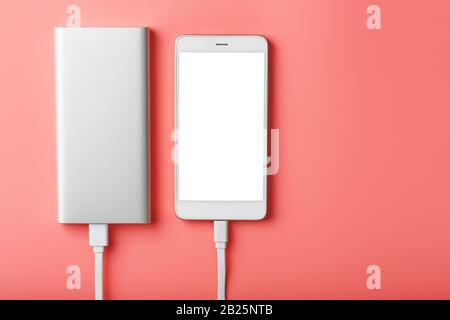 Powerbank carica uno smartphone su uno sfondo rosa. Batteria esterna universale per gadget spazio libero e composizione minimalista Foto Stock