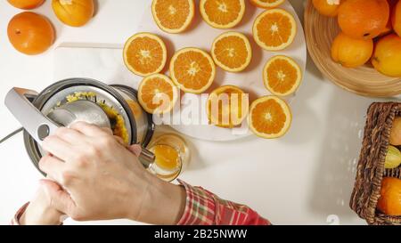 Succo d'arancia appena spremuto. Donna caucasica che spremono le arance utilizzando la centrifuga elettrica. Primo piano su sfondo bianco, vista dall'alto Foto Stock