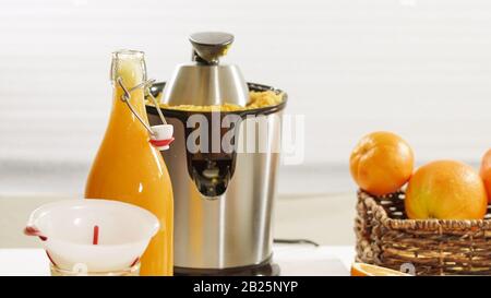 Succo d'arancia appena spremuto. Preparazione di succo d'arancia fresco con una centrifuga elettrica. Bottiglia di succo d'arancia da chiudere su un tavolo da cucina con ba bianca Foto Stock