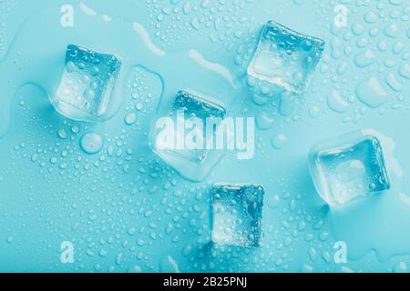 Cubetti di ghiaccio con gocce d'acqua sparse su uno sfondo blu, vista dall'alto. Ghiaccio rinfrescante. Foto Stock