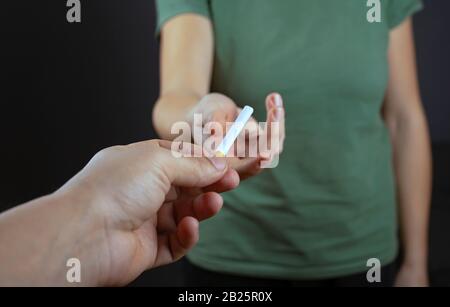 coccolati con una sigaretta. il ragazzo sta condividendo dà la ragazza su uno sfondo scuro. danno da fumo. Foto Stock